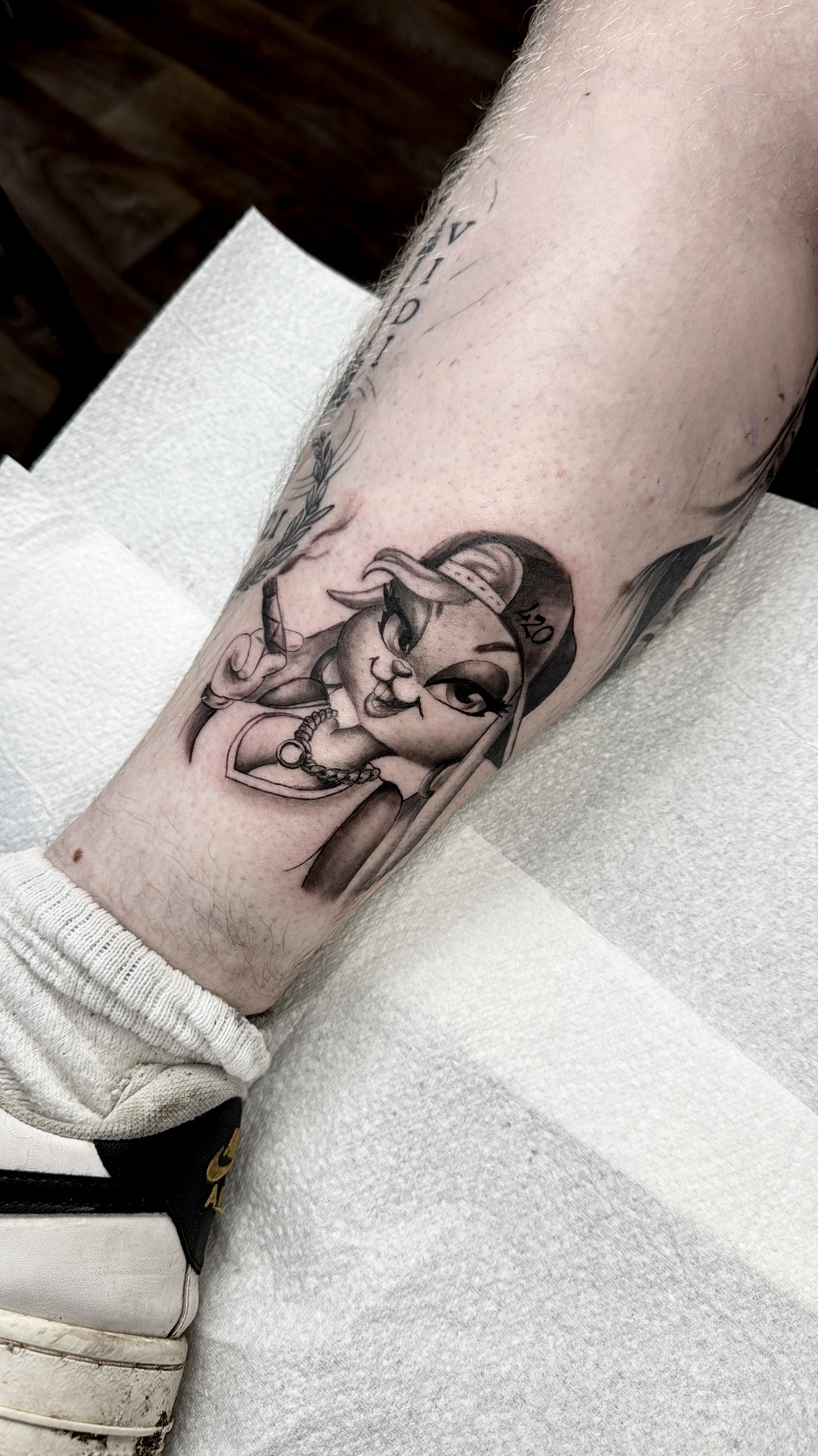 Black and grey illustrative tattoo of a cartoon rabbit character on the lower leg